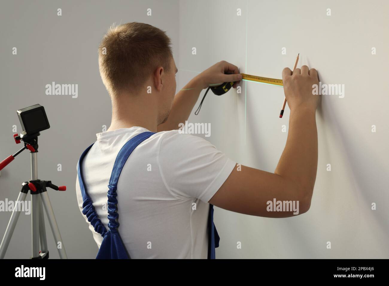 Arbeiter verwendet Kreuzlinienlaser-Nivelliergerät, Bleistift und Klebeband für genaue Messungen an leichten Wänden, Rückansicht Stockfoto
