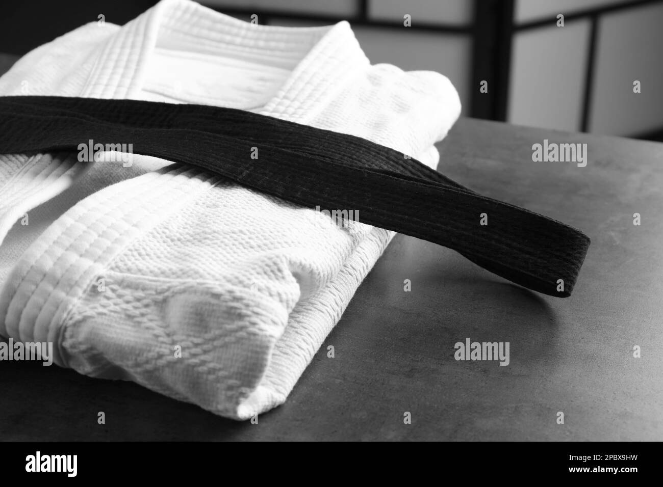 Kampfsport-Uniform mit schwarzem Gürtel auf grauem Steintisch drinnen Stockfoto