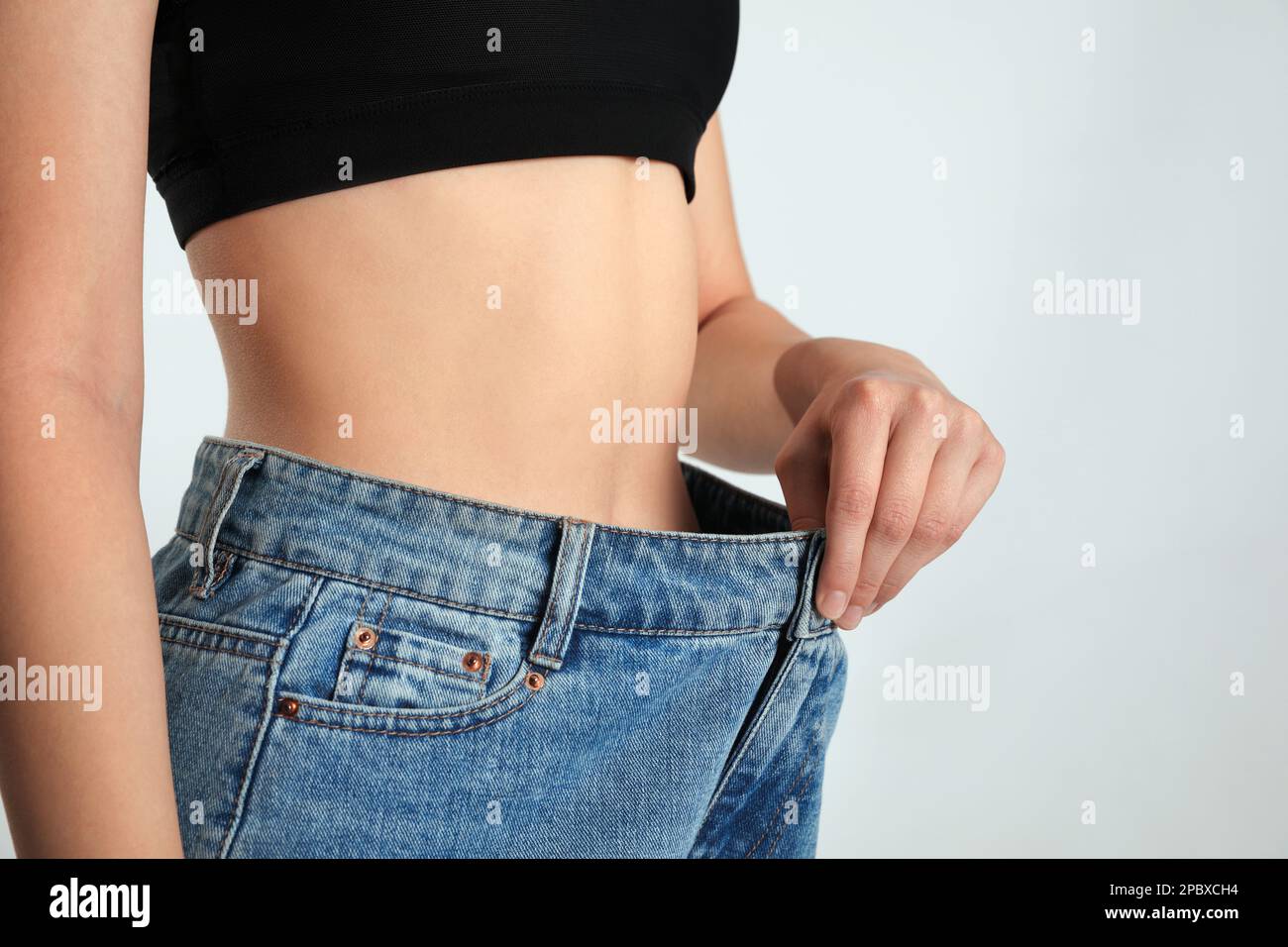 Dünne Frau in übergroßen Jeans auf hellem Hintergrund, Nahaufnahme. Gewichtsverlust-Konzept Stockfoto