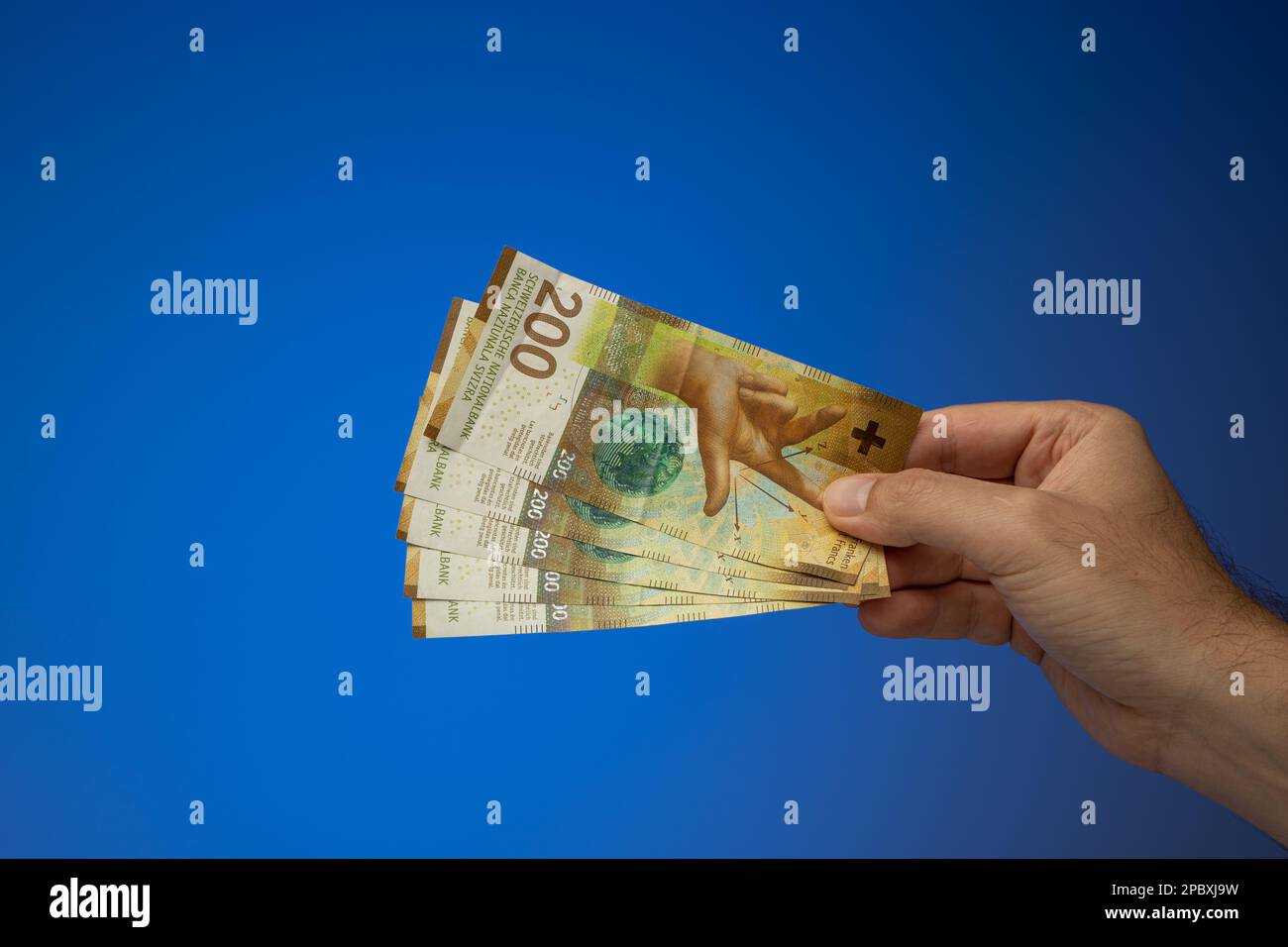 200 Schweizer-Franken-Banknoten, die ein weißer Mann in der Hand hält. Nahaufnahme des Studios, isoliert auf blauem Hintergrund. Stockfoto