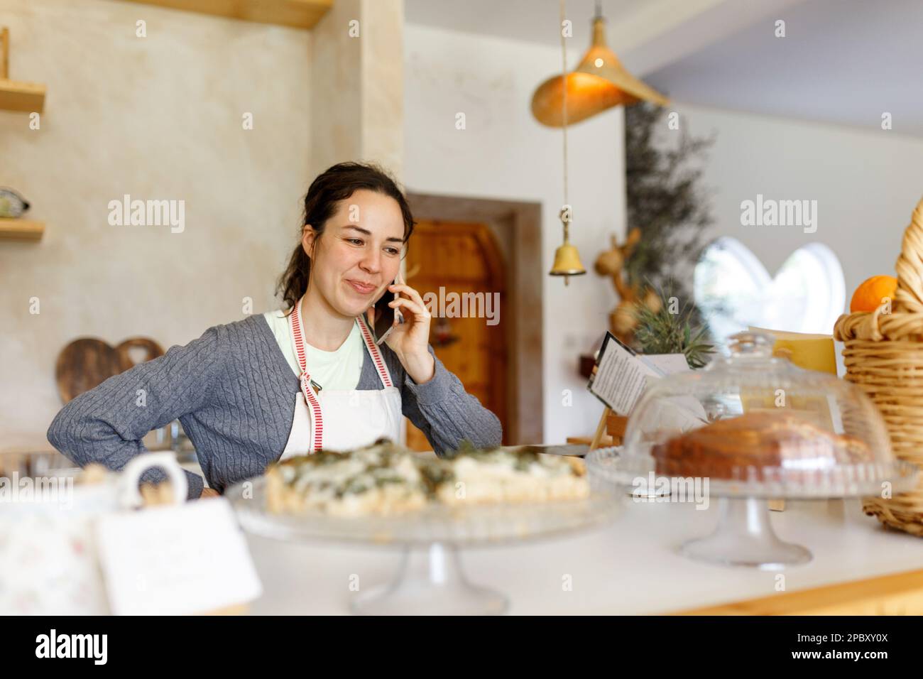 Glückliche junge Frau in der Schürze, Start-up wird wahr. Konzept für kleine Unternehmen. Familiengeschäft, Café-Laden. Telefonieren, Befehle entgegennehmen. Stockfoto