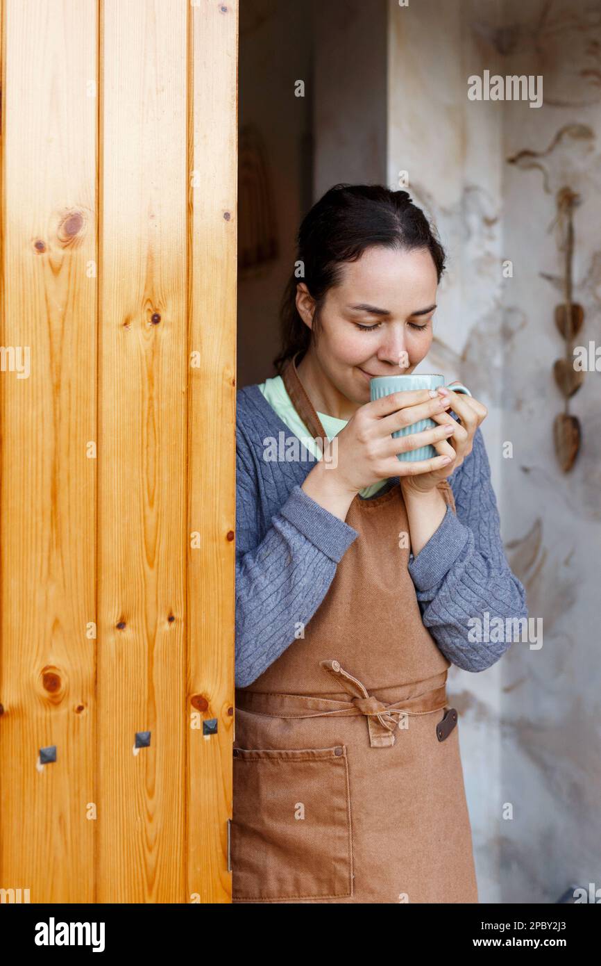 Junge Frau steht vor der Tür, Besitzer des Cafés, hält Becher und freut sich, dass das Start-up wahr wird. Konzept für kleine Unternehmen. Familiengeschäft, Café pla Stockfoto