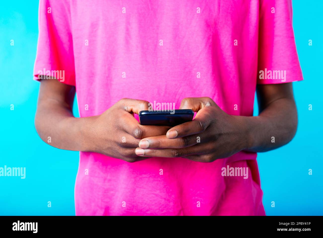 Ein unerkannter afroamerikanischer Typ in einem rosa T-Shirt, der vor blauem Hintergrund auf seinem Handy surft Stockfoto