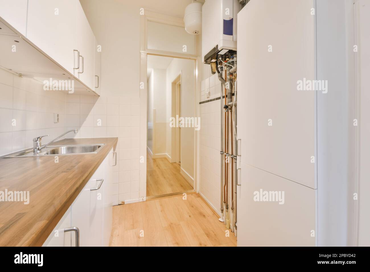 Zeitgenössisches Innendesign der geräumigen Küche mit weißen Schränken und Holzablagen mit Kühlschrank und Wasserkocher mit Waschbecken und Wasserhahn Stockfoto
