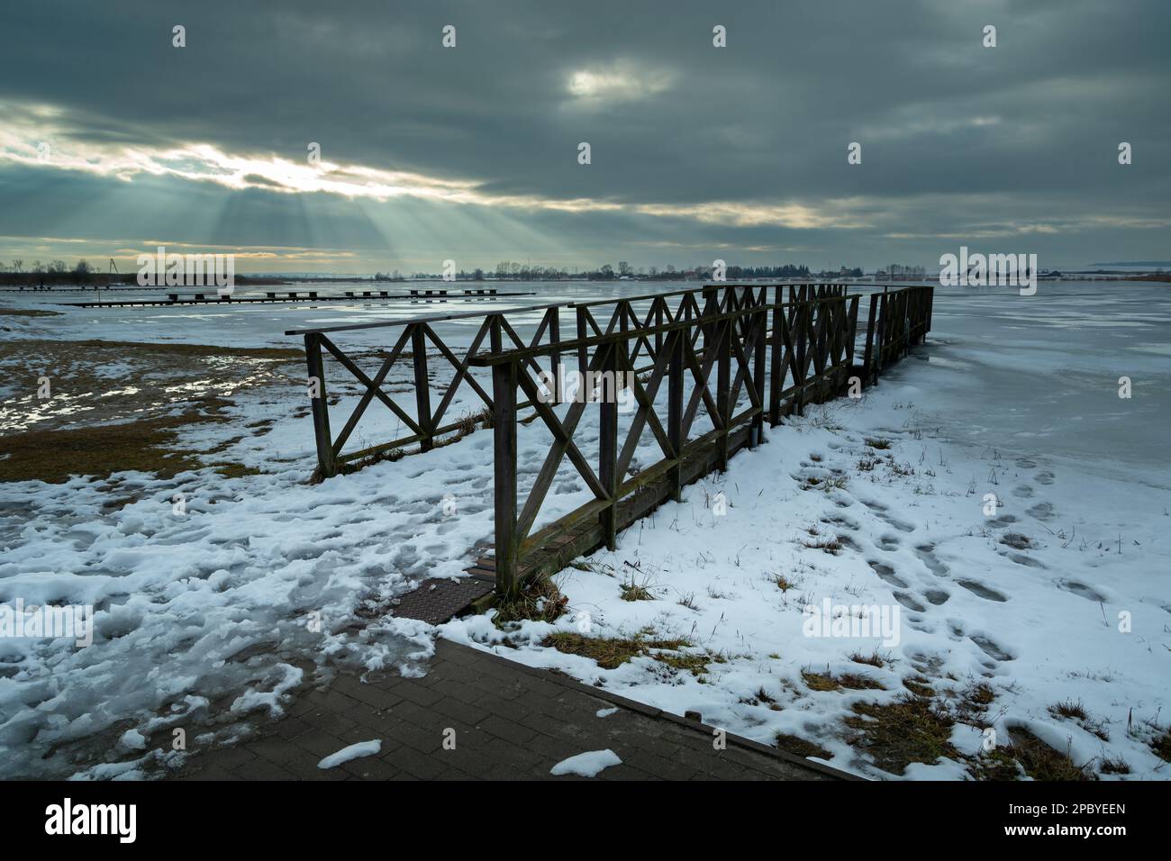 Winterblick auf einen hölzernen Pier und einen gefrorenen See, Sonnenbalken in den Wolken, Zoltance, Polen Stockfoto