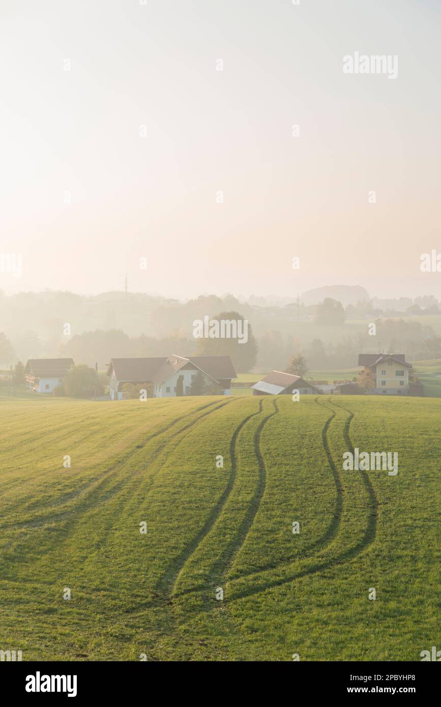 Landschaftsansicht des weiten Feldes mit Furchen in der Nähe des Dorfes Häuser unter Hügel bei Tageslicht in der Landschaft mit Nebel weit Weg Stockfoto