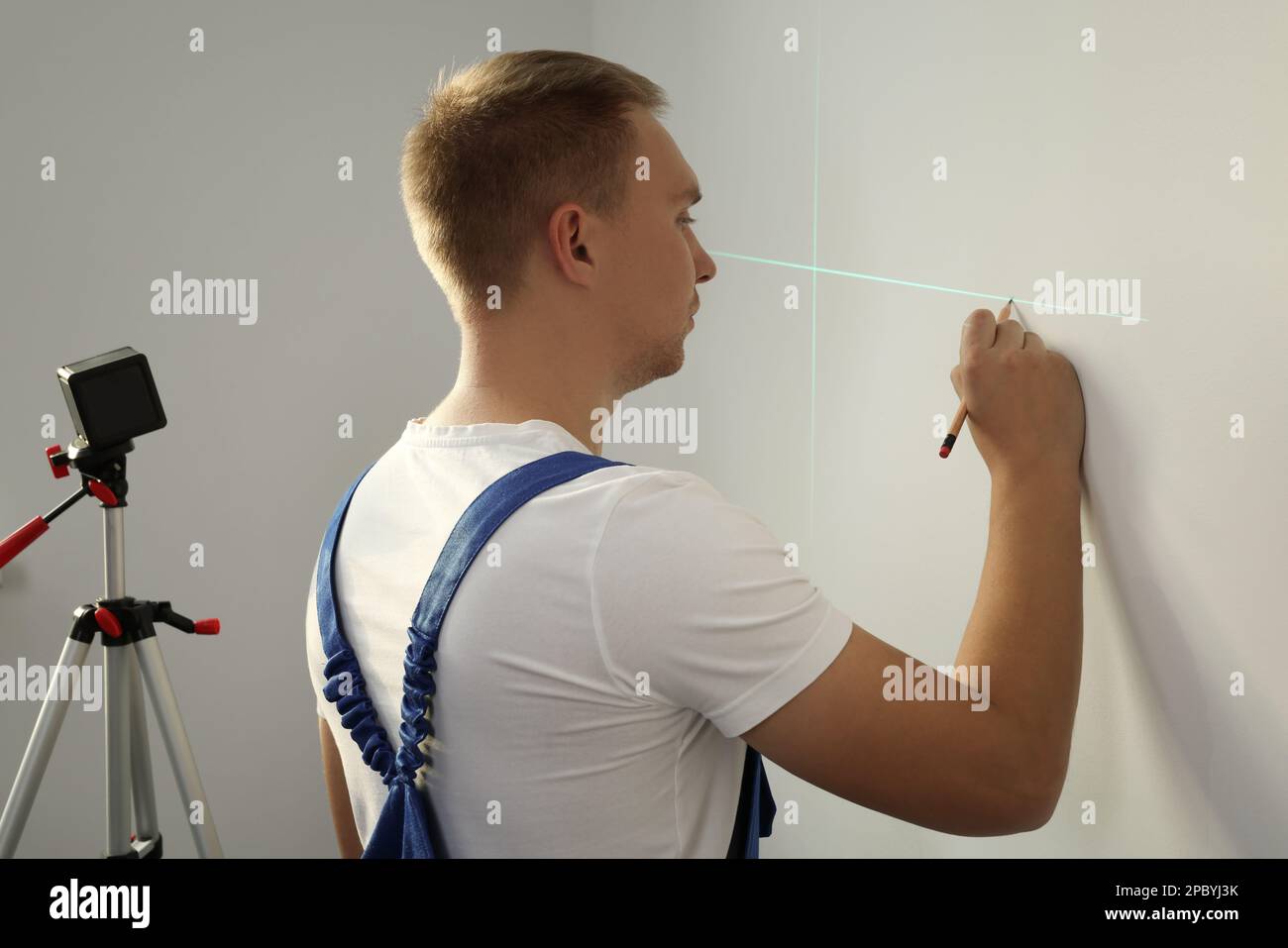 Arbeiter, der Kreuzlinienlaser-Nivelliergerät und Bleistift für genaue Messungen an hellen Wänden verwendet Stockfoto