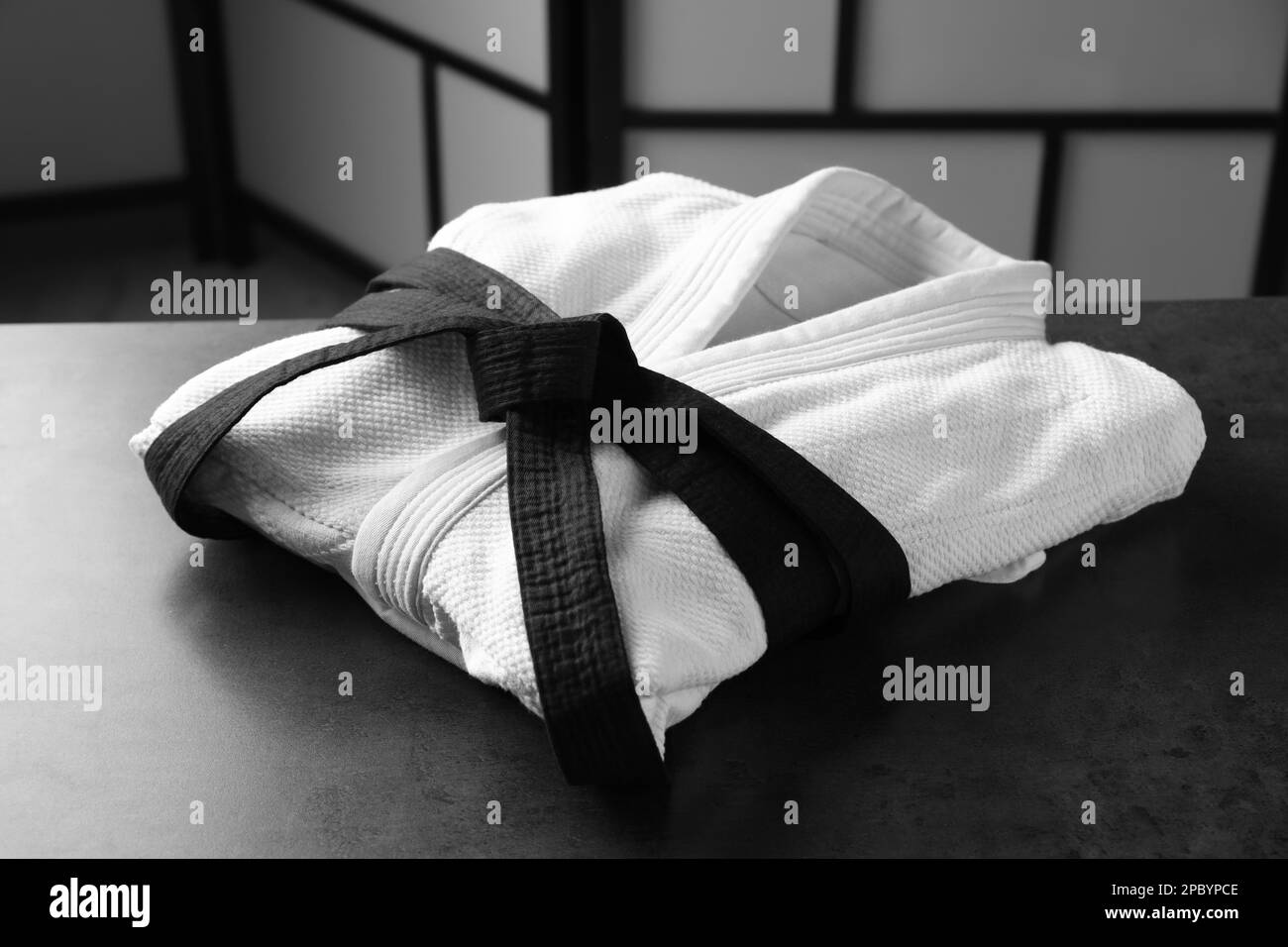 Kampfsport-Uniform mit schwarzem Gürtel auf grauem Steintisch drinnen Stockfoto