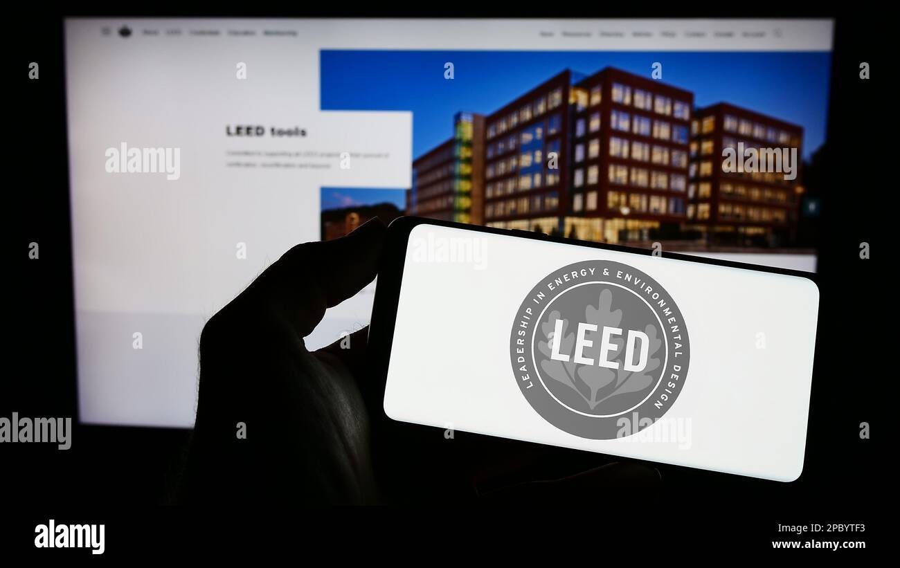 Person, die ein Mobiltelefon mit dem Logo der US-Umweltzertifizierung LEED auf dem Bildschirm vor der Webseite hält. Konzentrieren Sie sich auf das Display des Telefons. Stockfoto