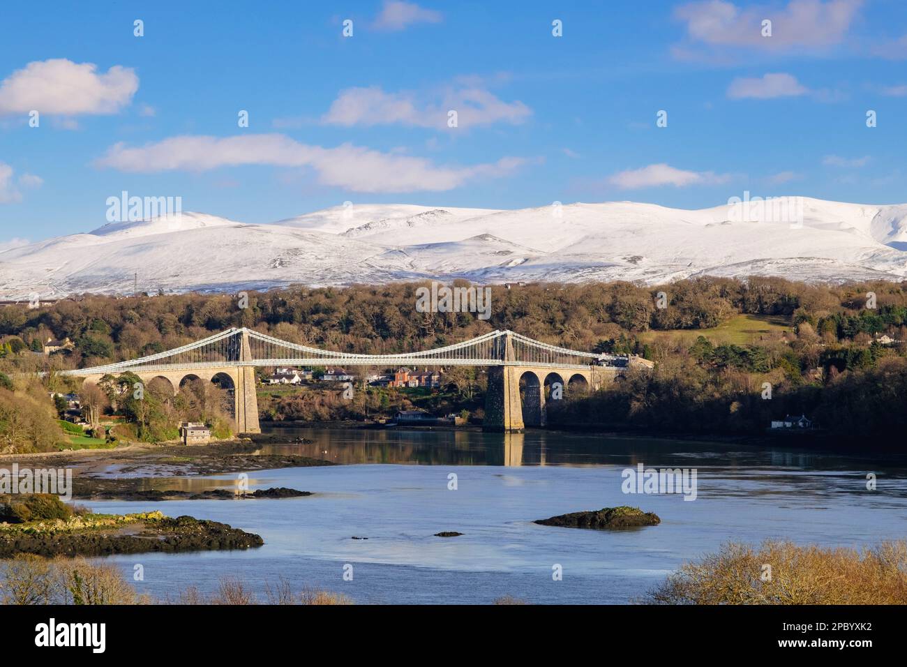 Malerischer Blick auf die Menai-Hängebrücke, die die Menai-Straße überquert, mit Schnee auf den Bergen im Winter. Menai Bridge (Porthaethwy), Isle of Anglesey, Wales, Vereinigtes Königreich Stockfoto