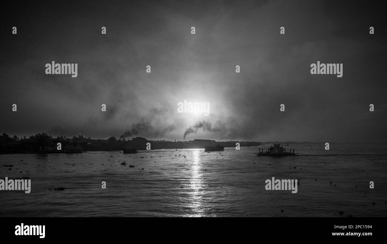 Eine Fähre überquert den Mekong bei Sonnenaufgang in der Nähe von Long Xuyen im Mekong-Delta in Vietnam, während Rauch aus Ziegelöfen entlang des Flussufers aufsteigt. Stockfoto