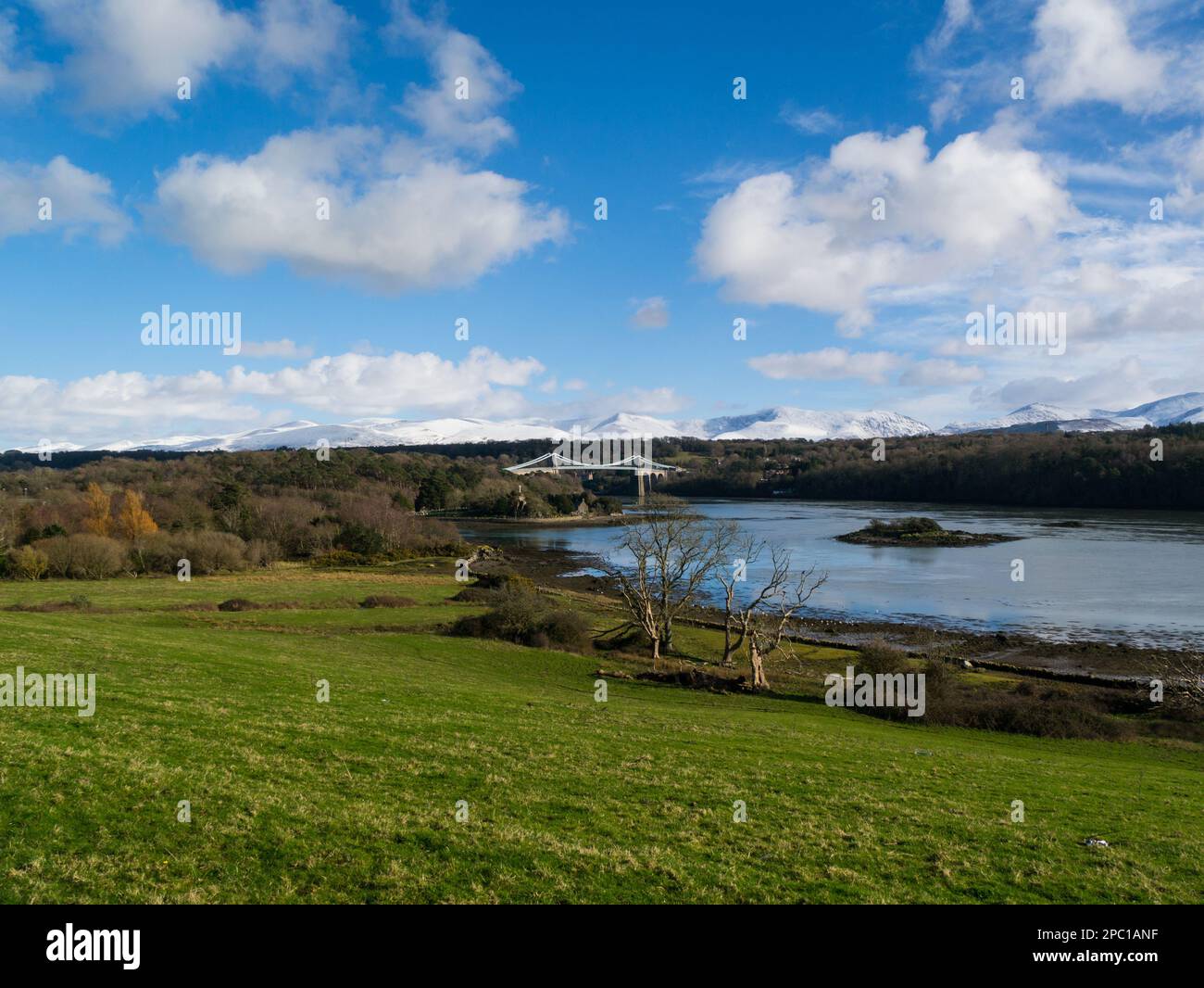 Blick über die Menai-Straße zur Menai-Brücke und Kircheninsel mit schneebedeckten Carneddau-Bergen im Hintergrund an hellen sonnigen Wintertagen Stockfoto