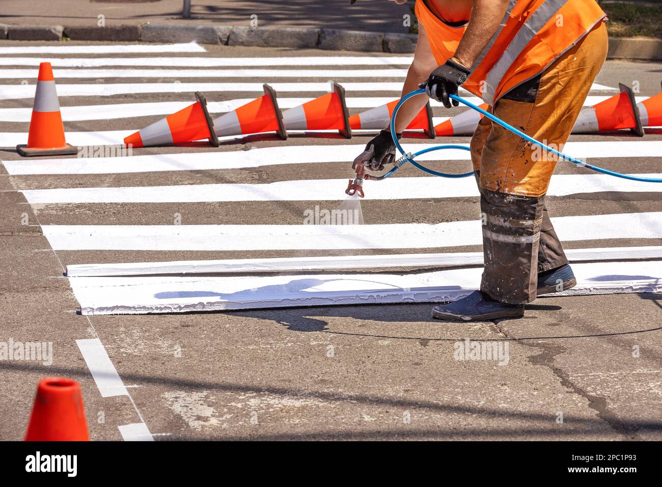 Ein Straßenarbeiter malt die Straße an einem Sommertag mit einer Sprühpistole auf einer Fußgängermarkierung. Stockfoto