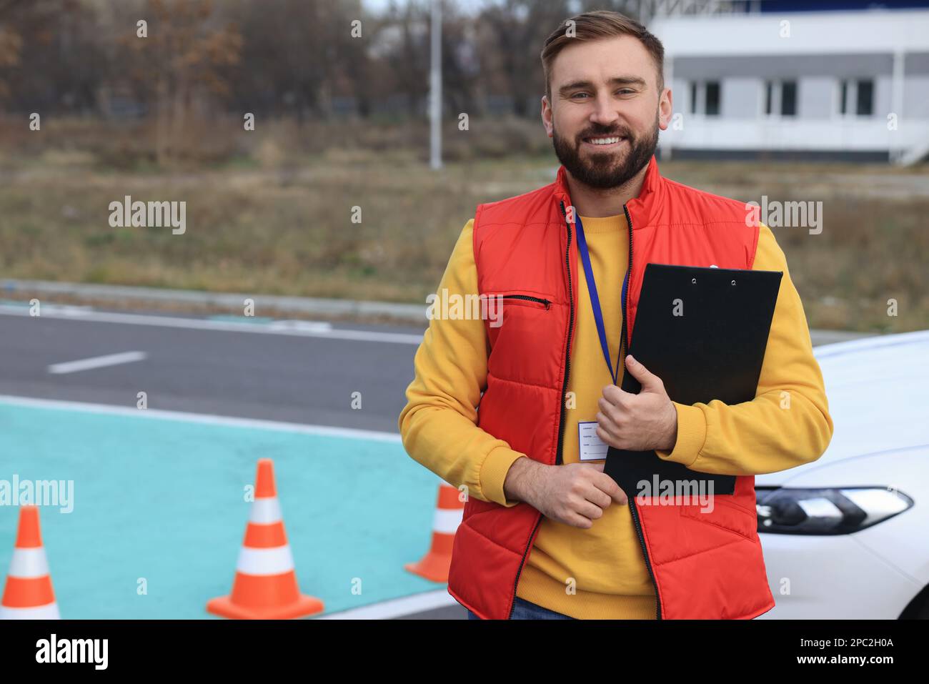 Kursleiter mit Klemmbrett in der Nähe des Fahrzeugs auf der Teststrecke. Fahrschule Stockfoto