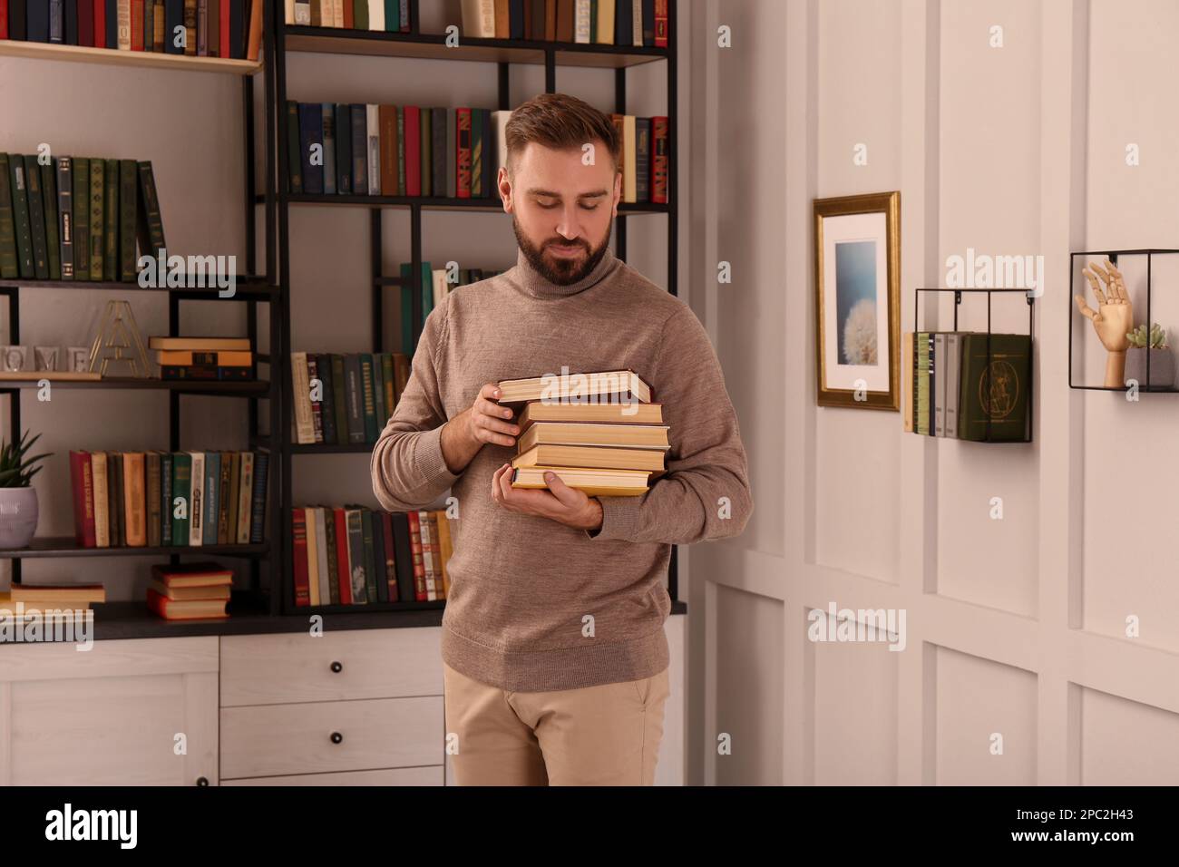 Junger Mann mit einem Stapel verschiedener Bücher in der Hausbibliothek Stockfoto