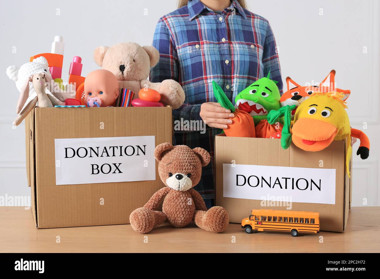 Kleiner Junge in der Nähe von Spendenboxen mit Spielzeug vor hellem Hintergrund, Nahaufnahme Stockfoto