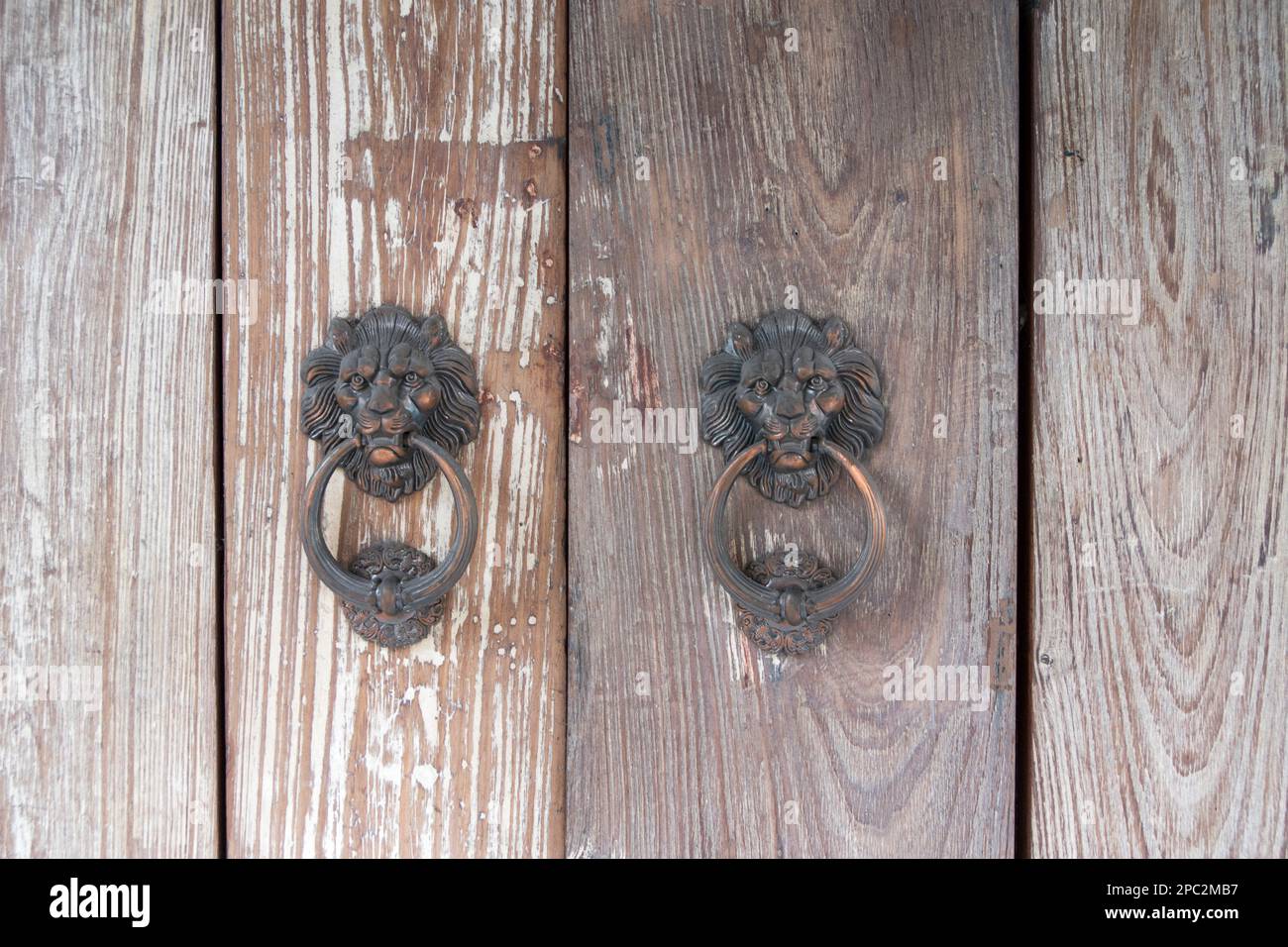 Nahaufnahme eines chinesischen Löwenknotens aus Metall an einer braunen Holztür Stockfoto
