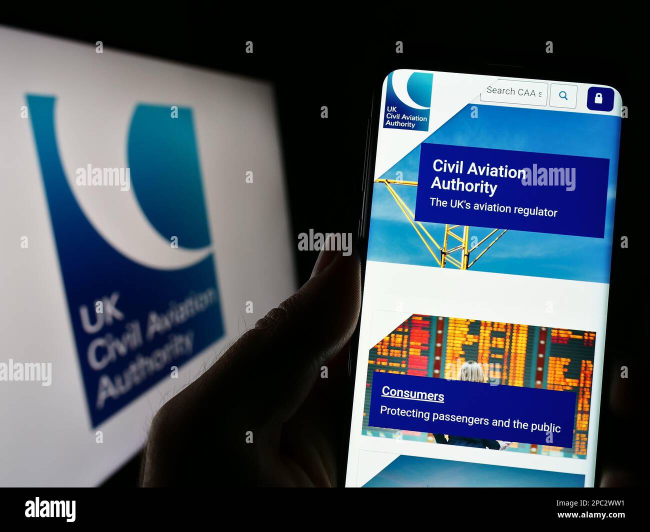 Person, die ein Mobiltelefon mit einer Website der britischen Regulierungsbehörde für Zivilluftfahrt (CAA) auf dem Bildschirm mit Logo hält. Konzentrieren Sie sich auf die Mitte des Telefondisplays. Stockfoto