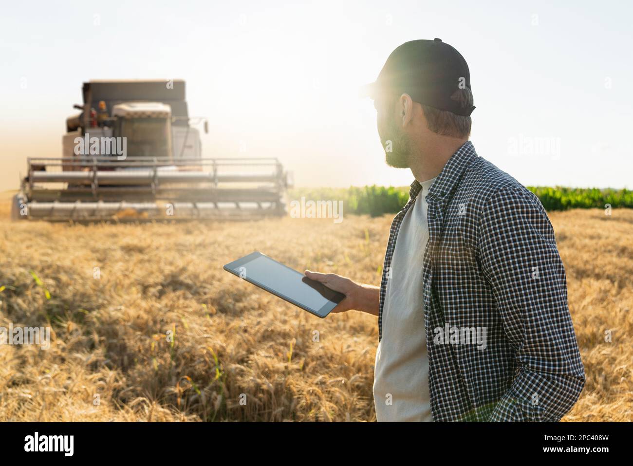 Landwirt mit digitalem Tablet auf dem Hintergrund des Mähdreschers. Smart Farming-Konzept. Stockfoto
