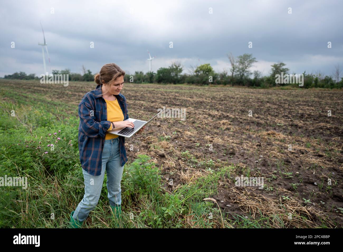 Bauer mit Laptop auf dem Feld. Windturbinen am Horizont. Intelligente, nachhaltige Landwirtschaft und Digitalisierung der Landwirtschaft Stockfoto