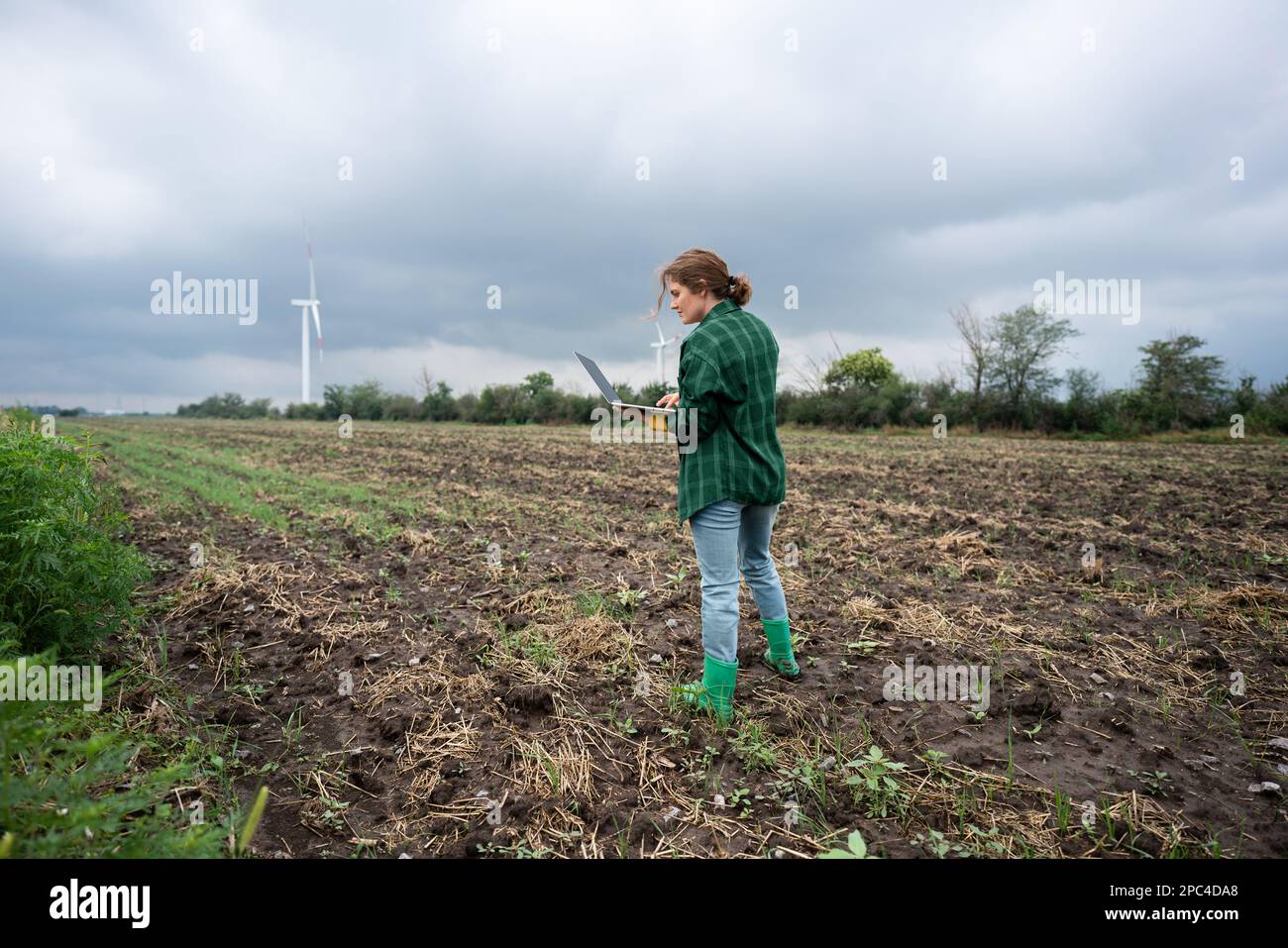 Bauer mit Laptop auf dem Feld. Windturbinen am Horizont. Intelligente, nachhaltige Landwirtschaft und Digitalisierung der Landwirtschaft Stockfoto