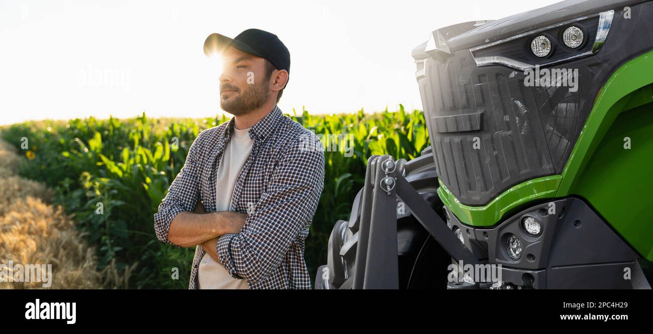 Ein bärtiger Bauer steht vor einem landwirtschaftlichen Traktor Stockfoto