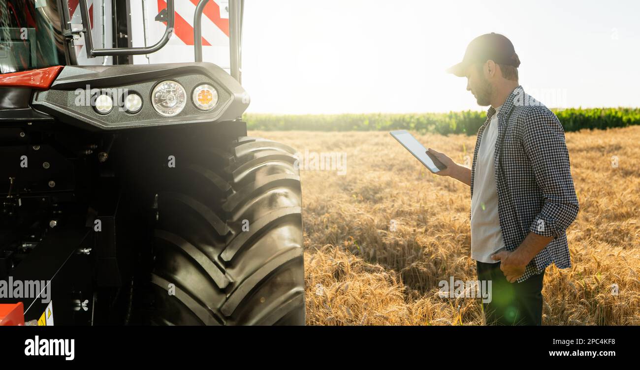 Landwirt mit digitalem Tablet steht neben dem Mähdrescher. Konzept der intelligenten Landwirtschaft. Stockfoto