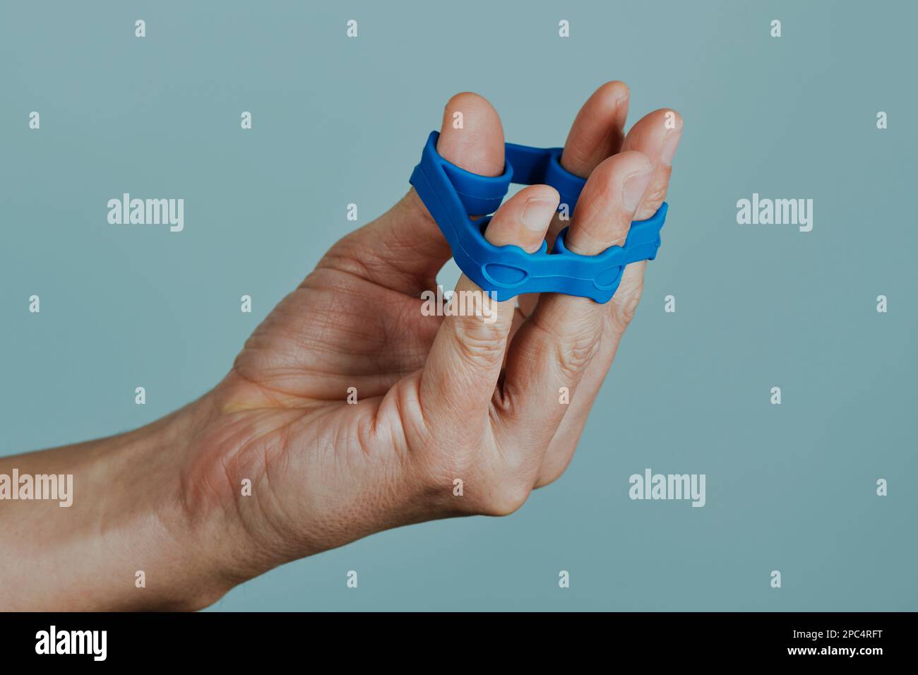 Ein Mann benutzt ein blaues Gummiband, um seine Finger vor einem hellgrauen Hintergrund zu bewegen Stockfoto