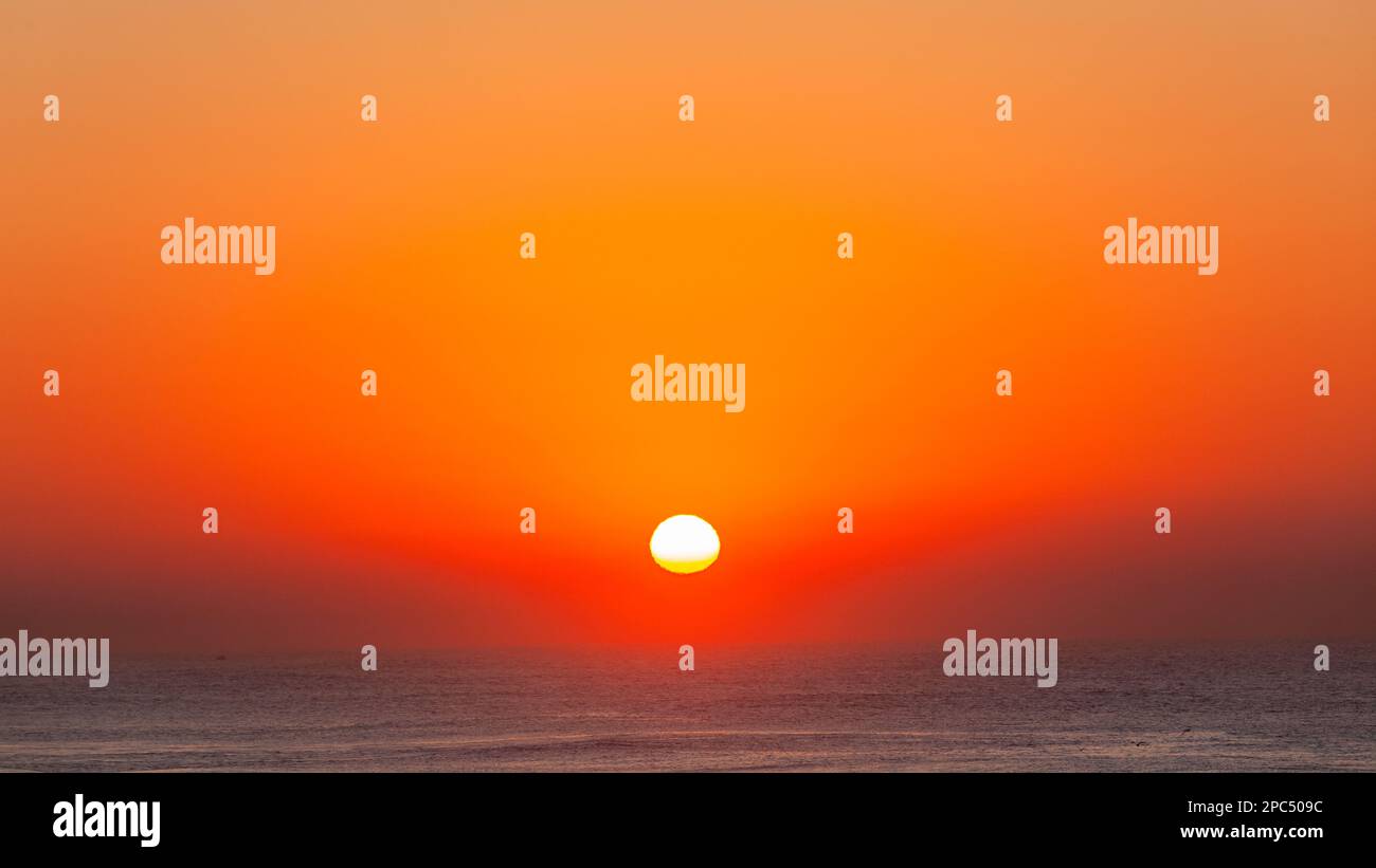 Ozeanhorizont mit Sonnenaufgang über der Wasseroberfläche des Ozeans in klarem Himmel mit einer Mischung aus rot-orangefarbenen Farben ein malerischer Moment der Natur. Stockfoto