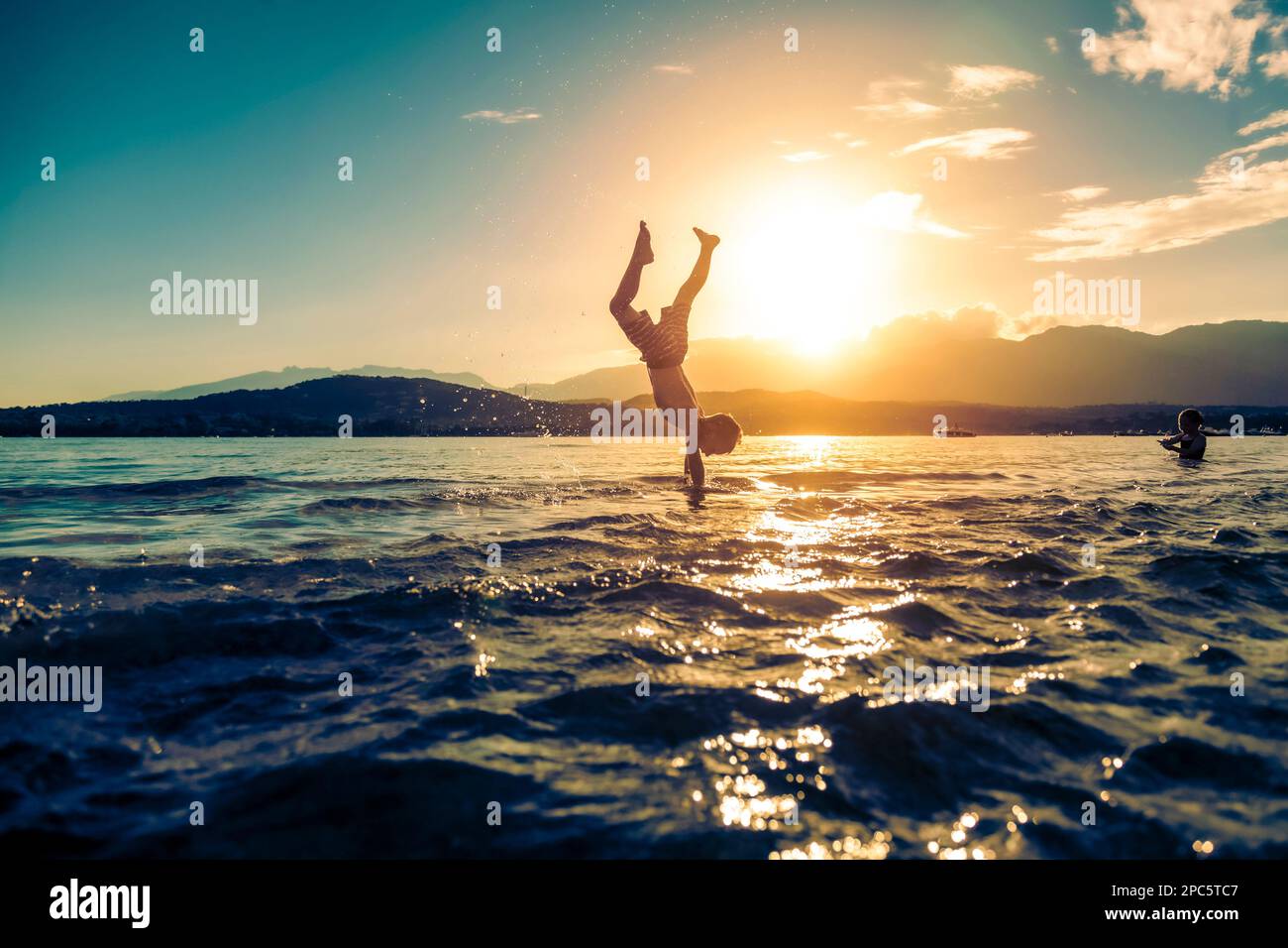 Das Kind spielt und hat Spaß im Meer und macht im Sommer Somersaults Stockfoto