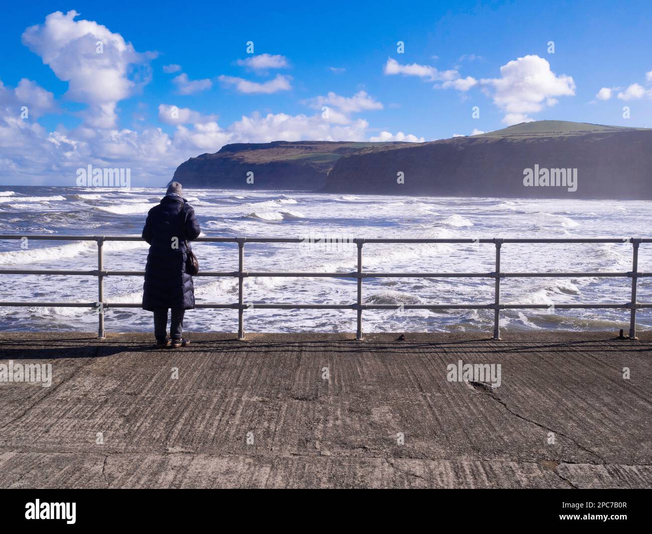 Von Woman mit Blick auf ein raues Meer von der Hafenmauer bei Skinningrove Überreste des Stegs, der früher von den Stahlwerken genutzt wurde, blicken Sie in Richtung Süden Stockfoto