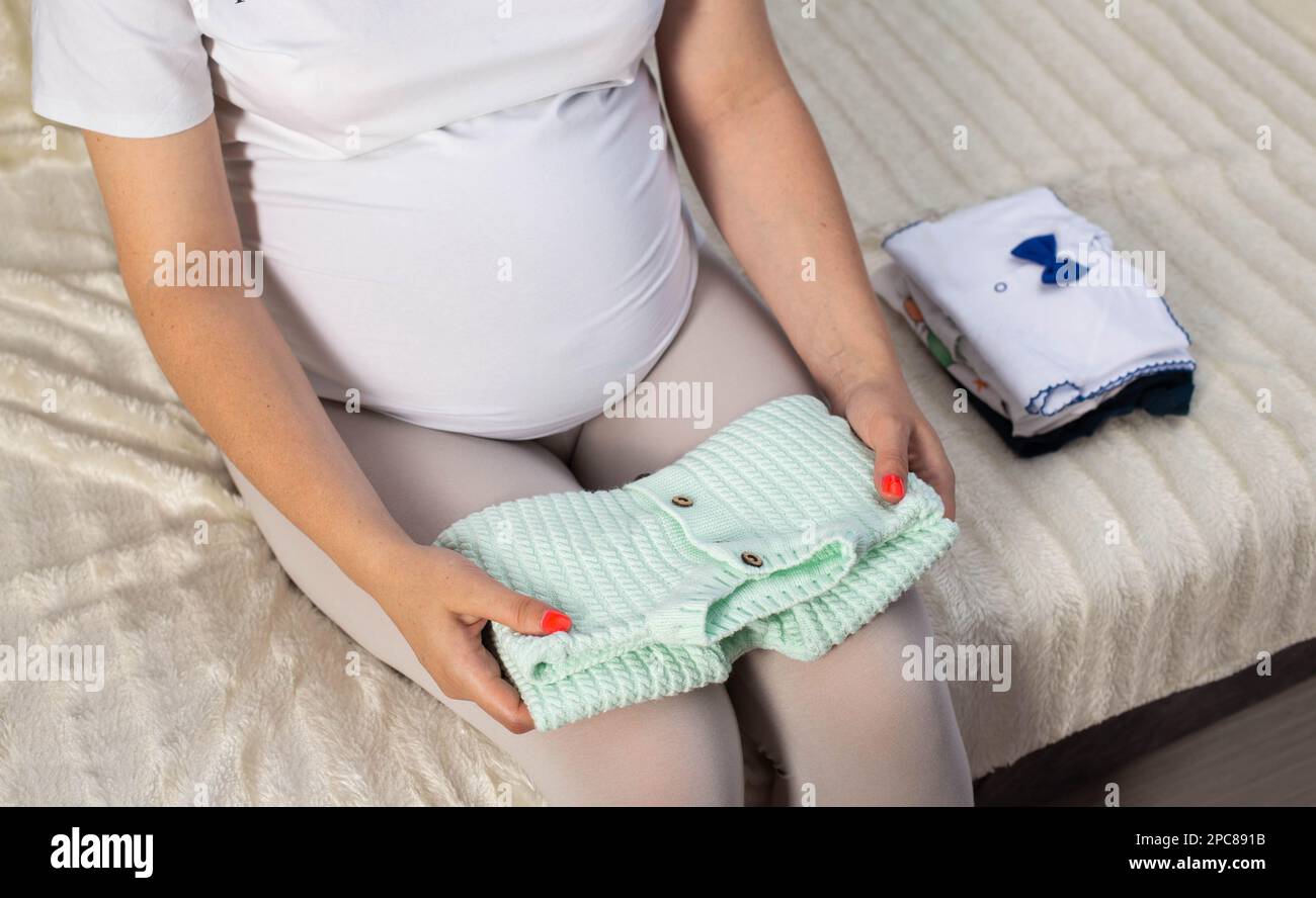 Ein schwangeres Mädchen sammelt Kleidung für ein Neugeborenes in der Entbindungsklinik. Stockfoto