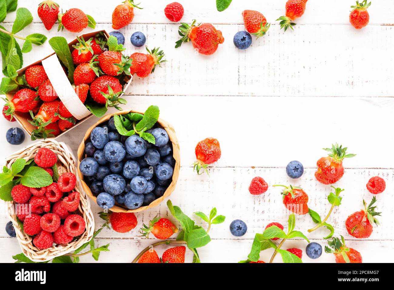 Verschiedene frische Beeren im Korb auf weißem Holzhintergrund, Draufsicht. Konzept der Sommerkost. Flach liegend, Kopierplatz. Stockfoto