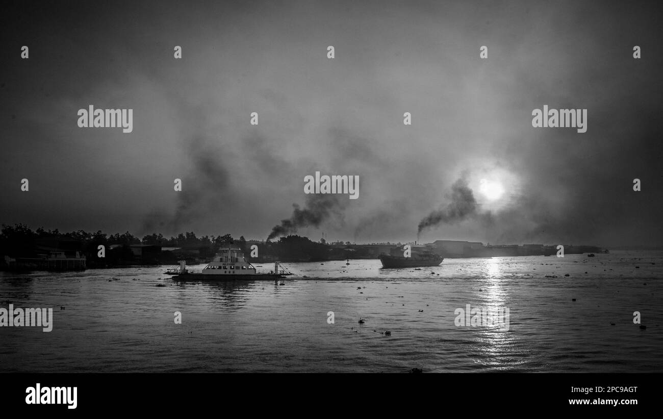 Eine Fähre überquert den Mekong bei Sonnenaufgang in der Nähe von Long Xuyen im Mekong-Delta in Vietnam, während Rauch aus Ziegelöfen entlang des Flussufers aufsteigt. Stockfoto