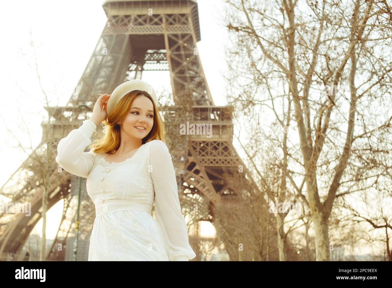 Ein Mädchen vor der Kulisse des Eiffelturms in Paris in einer Baskenmütze und einem Kleid mit lockigem Haar, eine romantische Reise. Eine Frau, die lacht und wegschaut Stockfoto