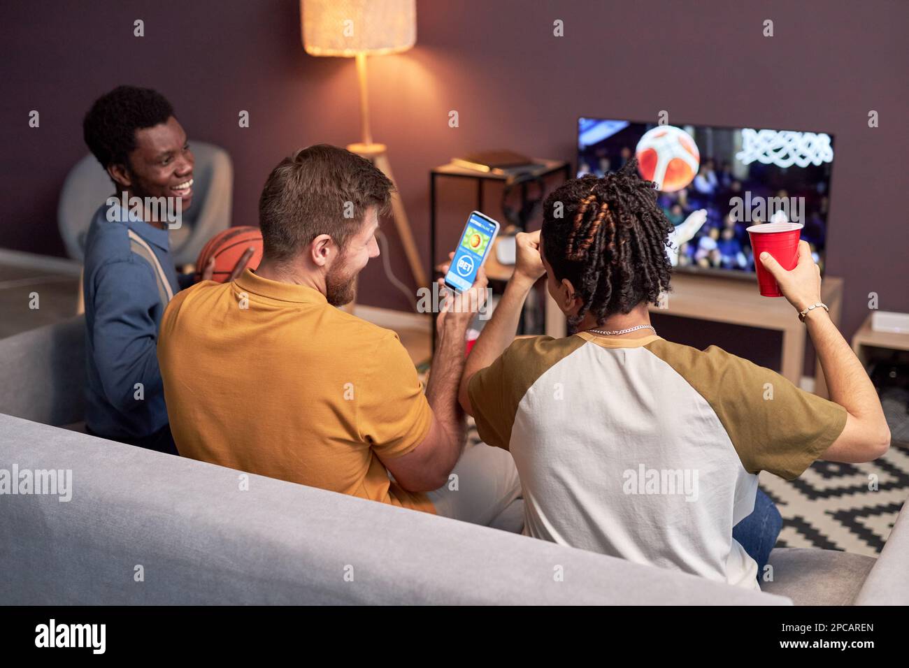 Eine Gruppe von Sportfans, die zu Hause ein Basketballspiel im Fernsehen sehen und jubeln Stockfoto