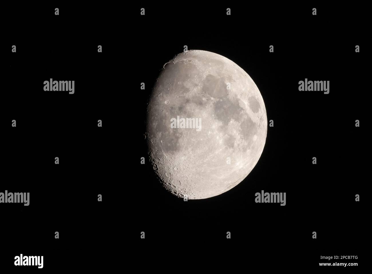 Teleeinstellung eines dreiviertel Mondes Ende Februar 2023 mit Bergen und Stute gegen den schwarzen Himmel Stockfoto