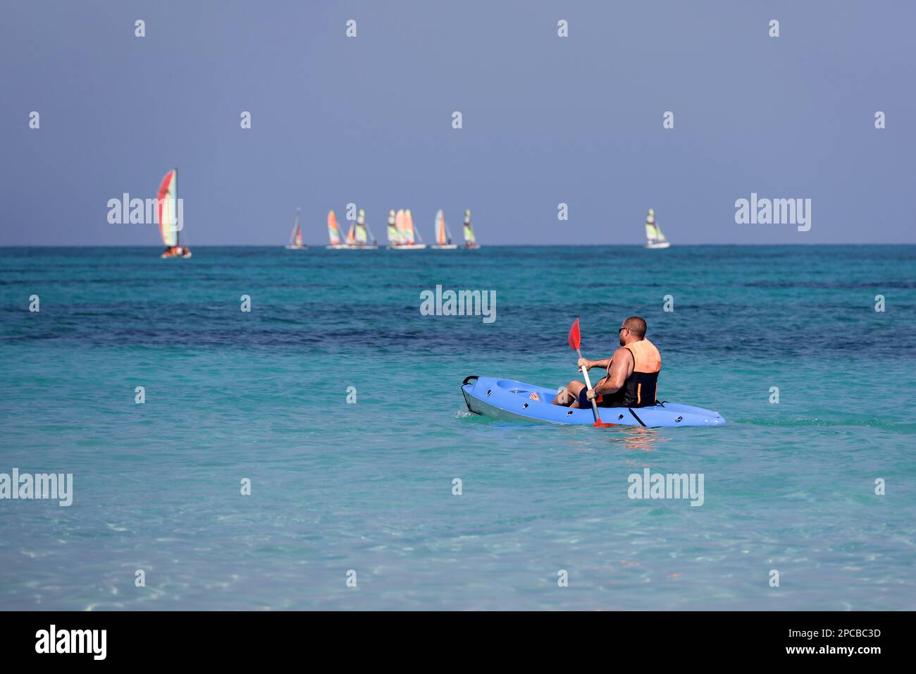Kajakfahren auf dem Meer, Mann mit Schwimmweste rudert mit einem Ruder im Kanu auf Segelbooten im Hintergrund. Reise- und Wassersportkonzept Stockfoto