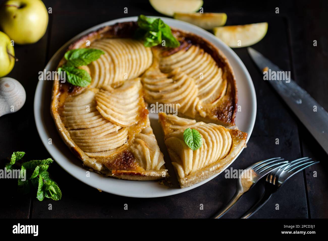 apfelkuchen: Versuchung auf schwarzem Hintergrund. Traditioneller offener Kuchen mit dünnen Äpfelstücken, dekoriert mit Minzblättern. Stockfoto