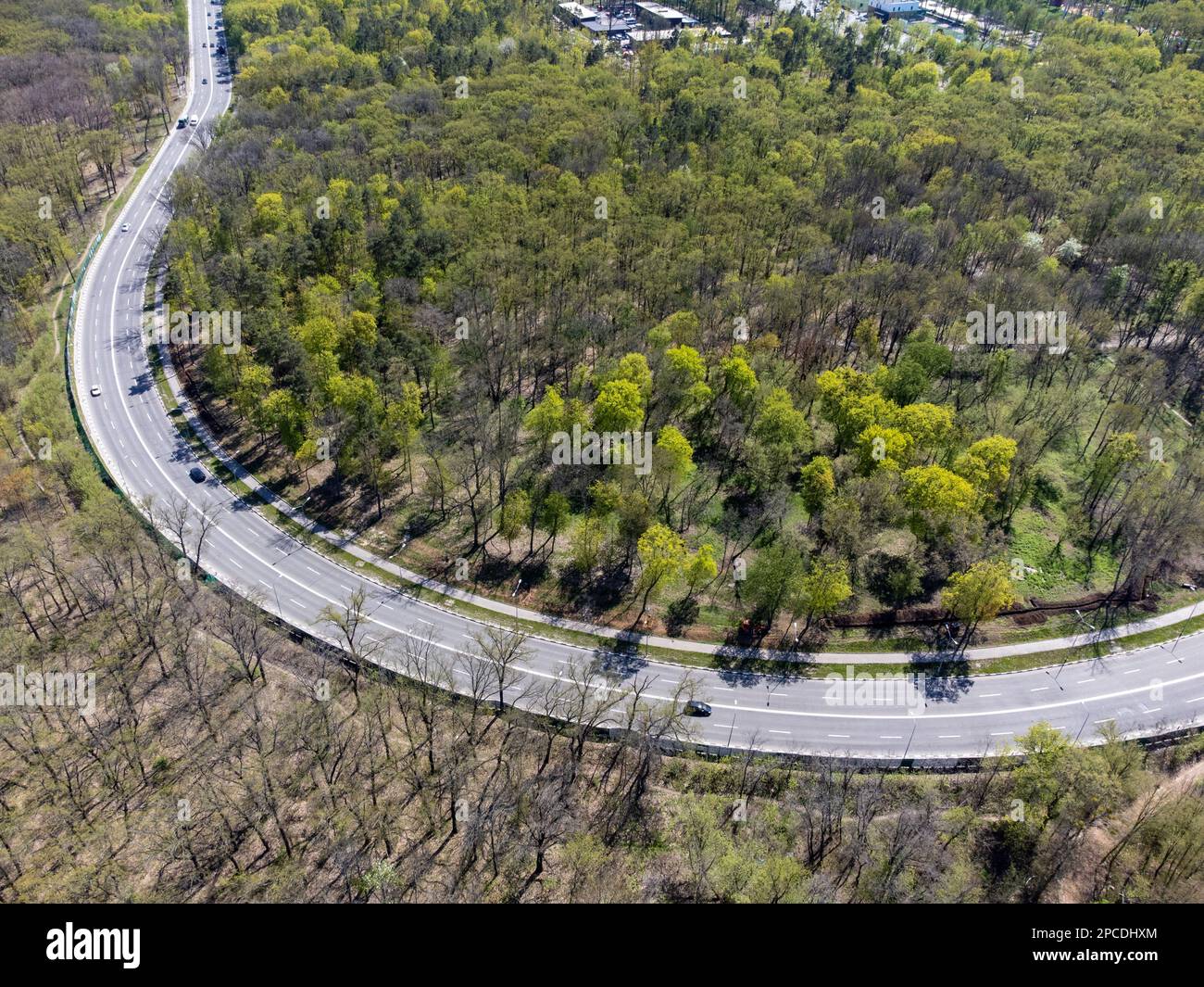 Von der Luft aus blickt man auf die Highway Road, die von Wäldern mit jungen grünen Blättern umgeben ist. Charkiv Stadtstraßen Stockfoto