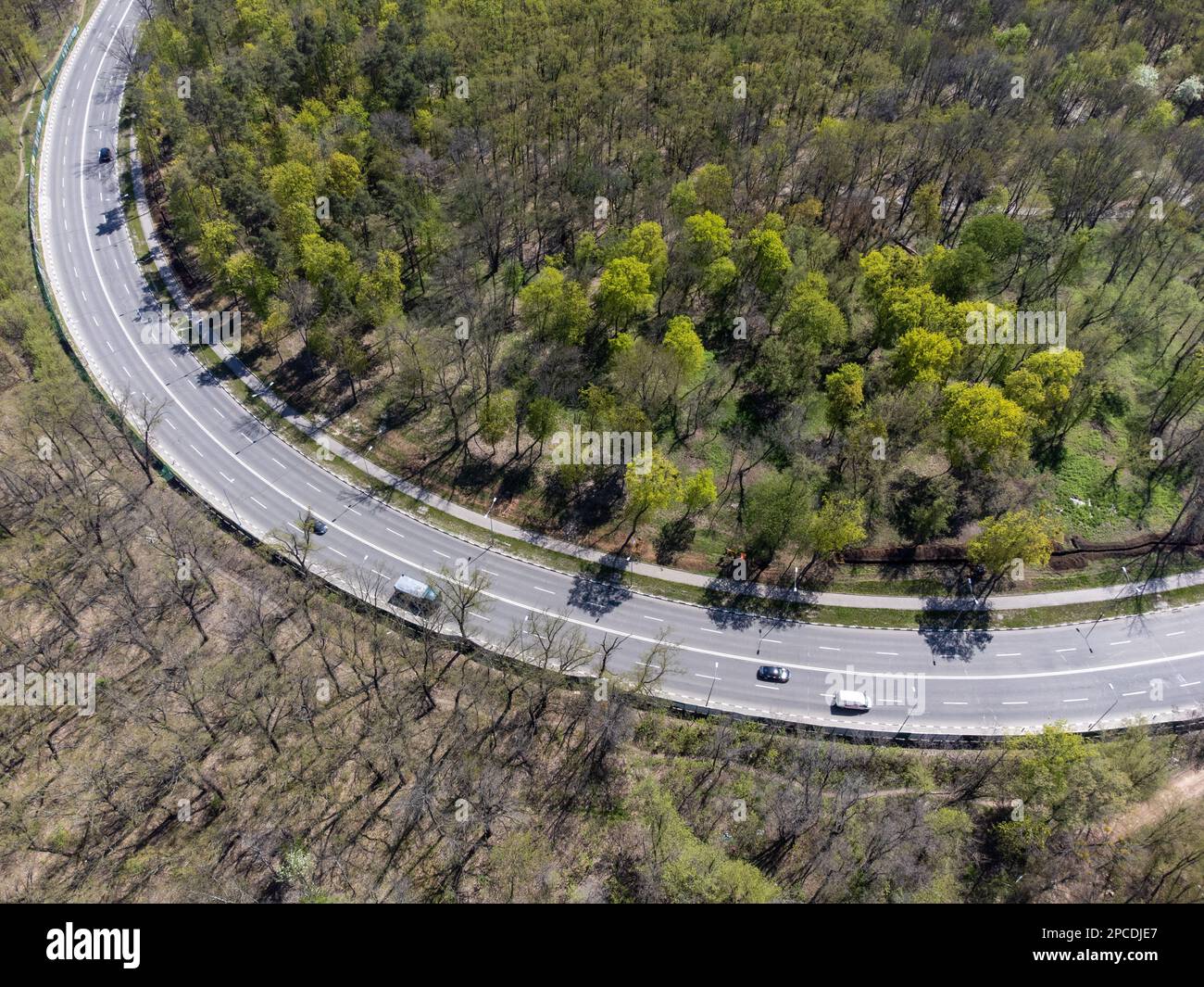 Blick von oben nach unten auf die Autobahnkurve im Wald mit jungen Grünflächen. Charkiv Stadtstraßen Stockfoto