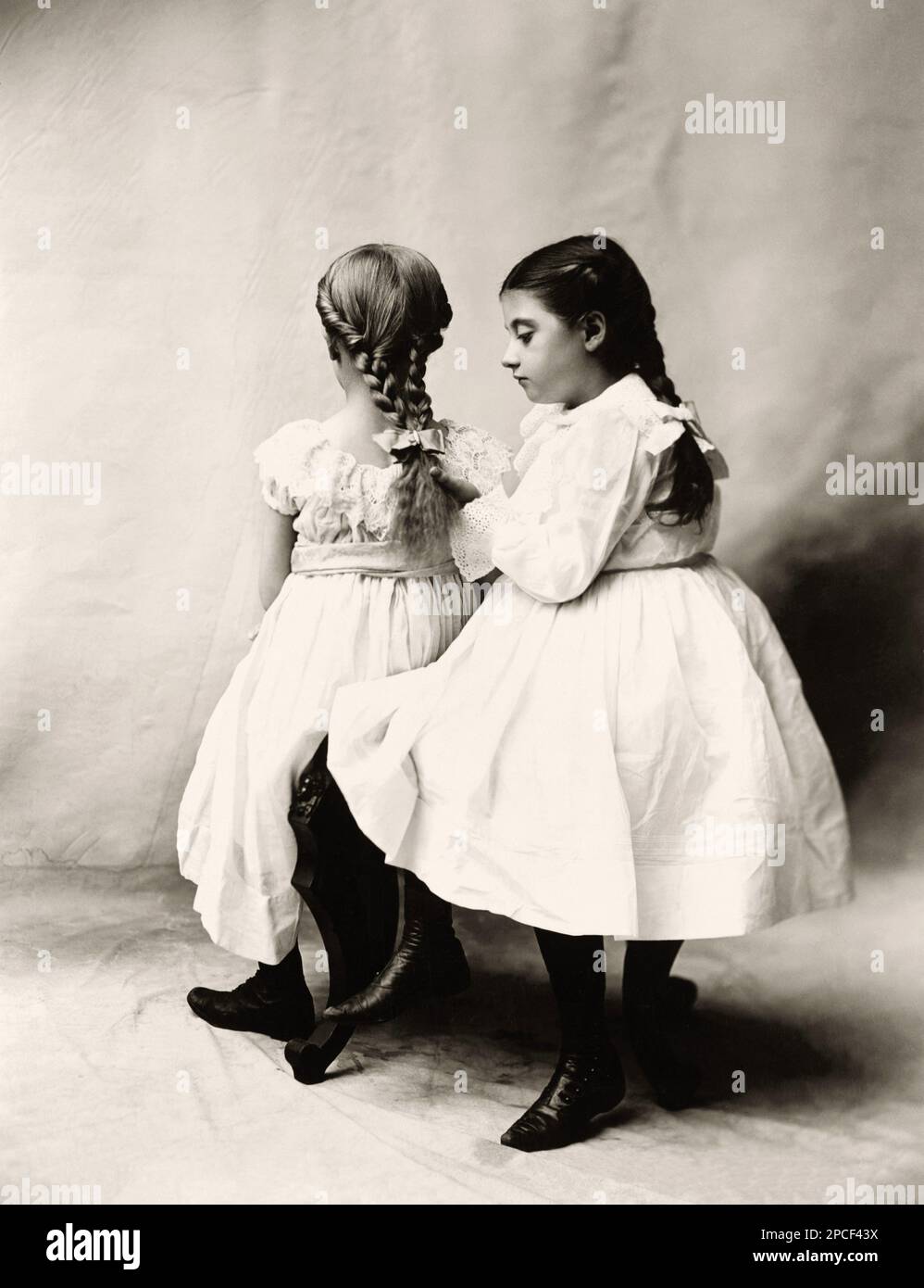 1900 , Chicago , USA : The Sisters . Zwei Mädchen sitzen, eine schaut sich geflochtene Haare an. Foto: Tonnesen Sisters, Chicago .- DUE SORELLE - FOTO STORICHE - HAIR - CAPELLI - TRECCIA - TRECCIE - ACCONCIATURA - ACCONCIATURE - FIOCCO - BUG - GESCHICHTSFOTOS - weißes Kleid - abito vestito bianco - Schuhe - Scarpe - NOVECENTO - 900 's - '900 - BELLE EPOQUE - - Kind - BAMBINA - BAMBINA - BAMBINO - BAMBINI - KINDER - BABY - KINDHEITSKINDHEIT ---- Archivio GBB Stockfoto