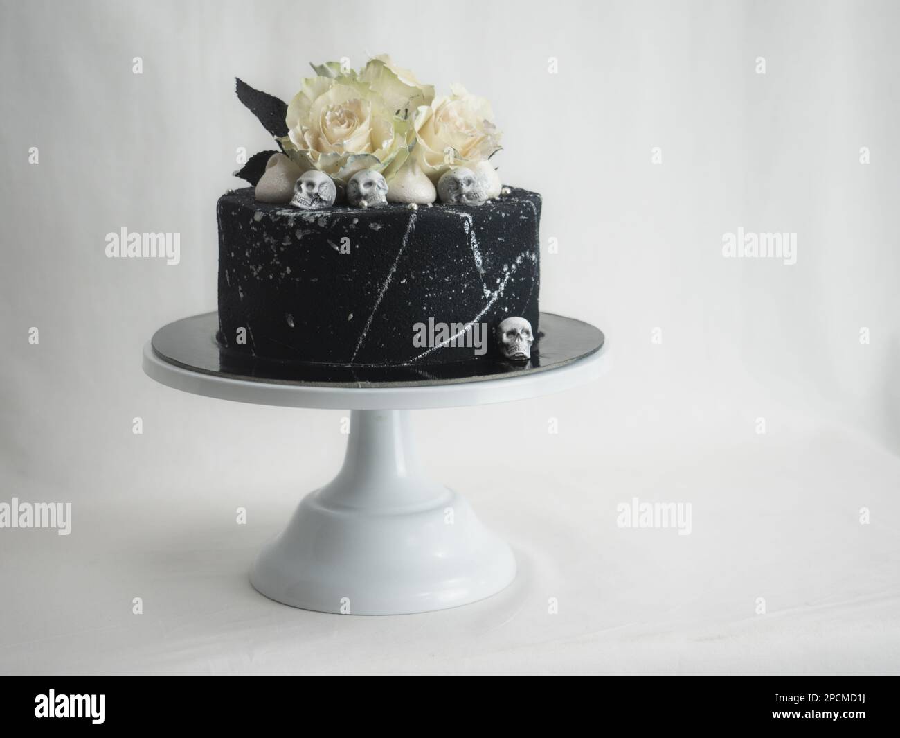 Geburtstagskuchen mit schwarzem Airbrush-Maler, Milchkuchen, zwei silberne Rosen, versprühte und essbare Schokoladenköpfe und silberne Pinselstriche Stockfoto