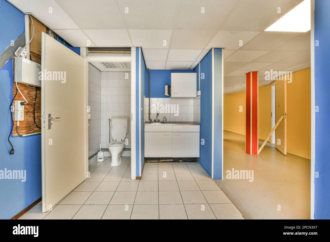 Ein leeres Bad mit blauen Wänden und weißen Fliesen auf dem Boden, von der Tür zur Toilette aus gesehen Stockfoto