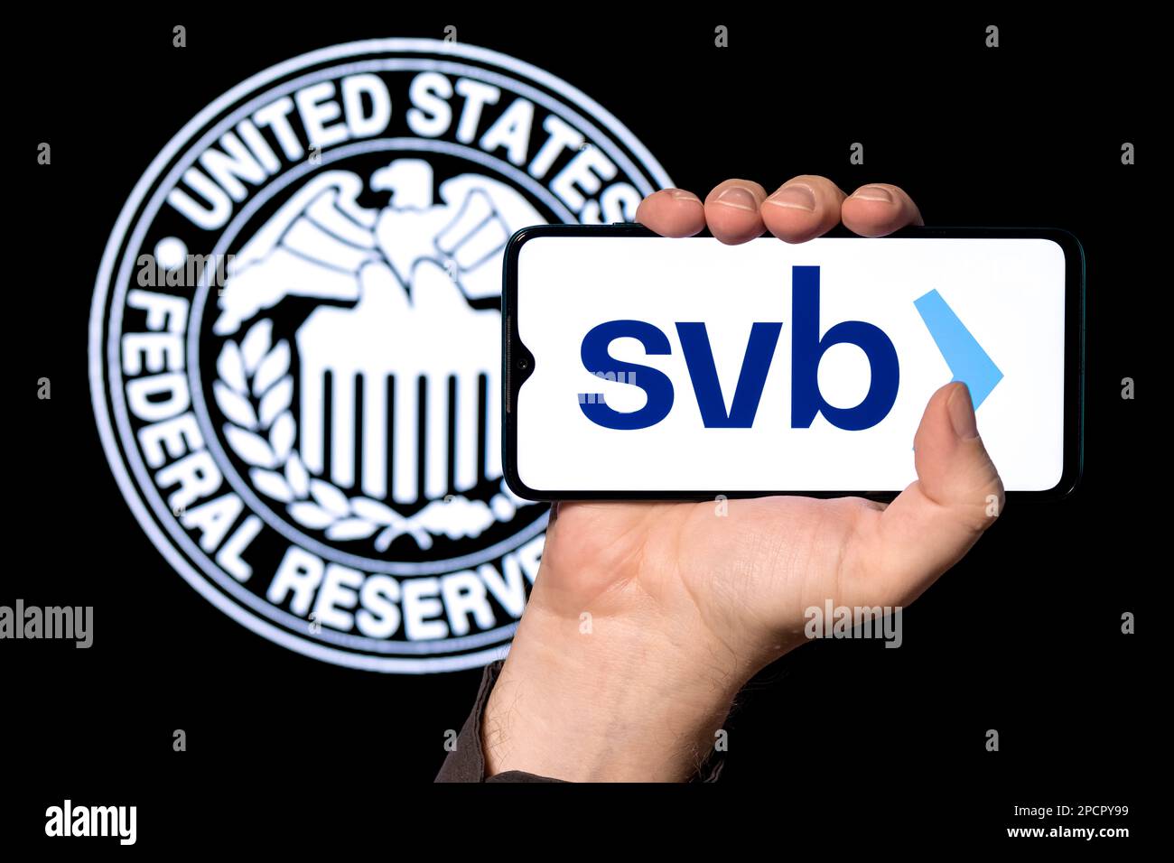 Smartphone mit Silicon Valley Bank Logo in geballter Hand auf dem Hintergrund des Federal Reserve Symbols Stockfoto