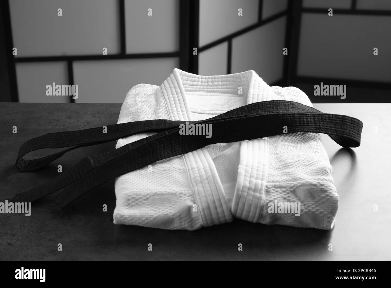 Kampfsport-Uniform mit schwarzem Gürtel auf grauem Steintisch drinnen Stockfoto