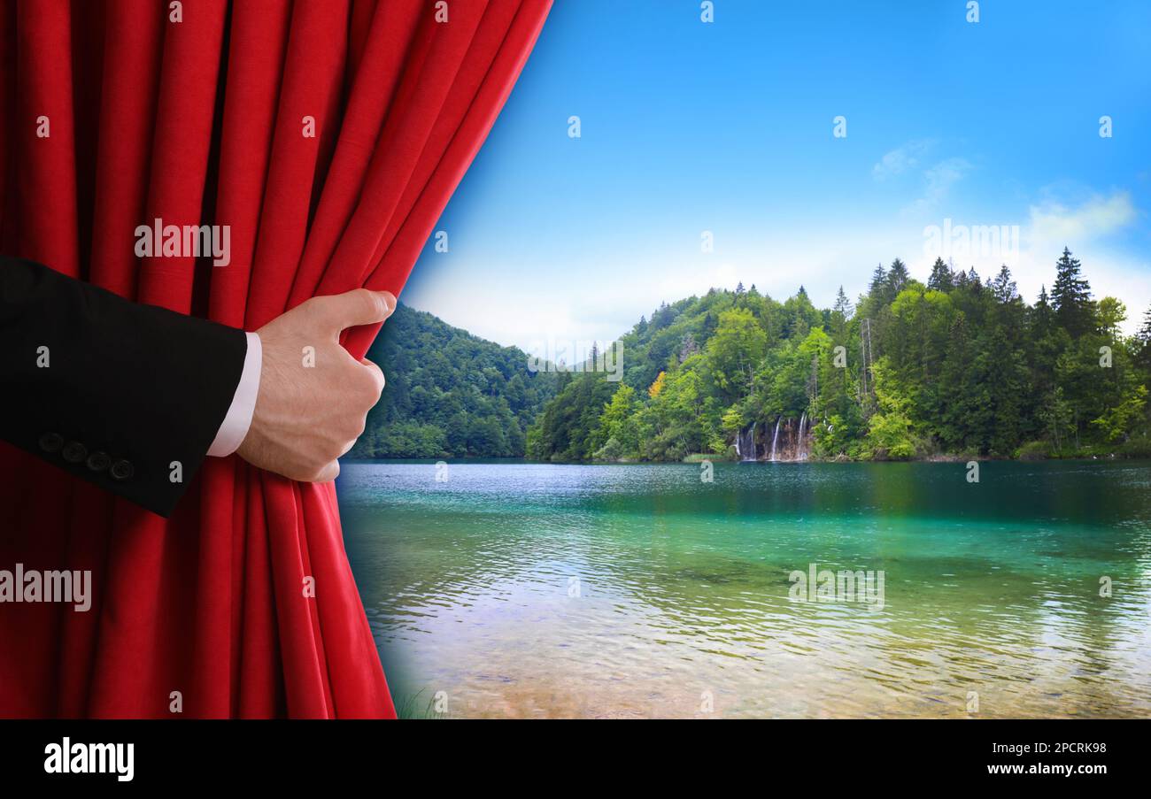 Ein Mann öffnet den roten Vorhang und bietet einen malerischen Blick auf den Fluss und die Berge im Hintergrund Stockfoto