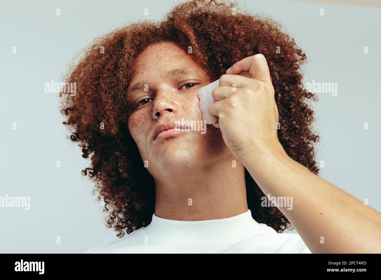 Ein junger Mann, der sein Gesicht mit einem Gua-sha-Stein massiert, um Schwellungen zu reduzieren und sein Aussehen zu verbessern, bringt seine Pflege auf ein neues Niveau. Mann mit fr Stockfoto