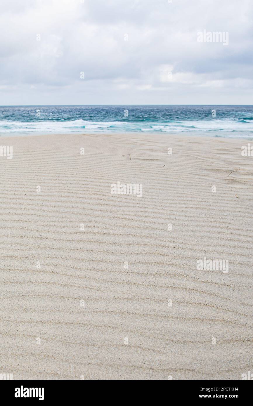 Weiße Sanddünen und die Muster von Wellen im Sand mit dem pazifischen Ozean dahinter, eine minimalistische Szene in Aotearoa Neuseeland. Stockfoto