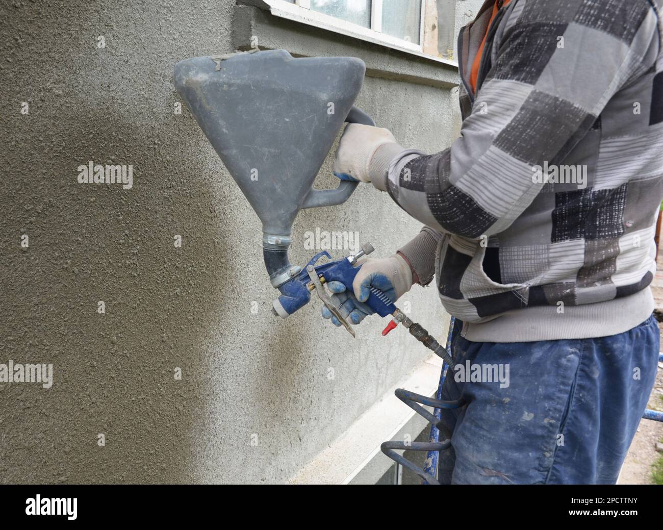 Ein Bauunternehmer verputzt, verputzt und beschichtet die Außenwand eines Gebäudes mit einer Putzsprühmaschine und einer Betonsprühpistole aus Stuck. Stockfoto